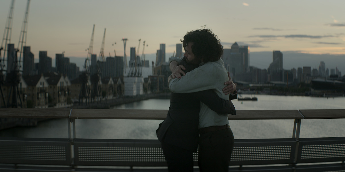 Penn Badgley and Ed Speleers hug on a footbridge as Rhys and Joe