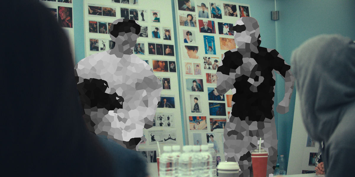 People gathered in a meeting room with a wall covered in photographs, water bottles on the table, some individuals are pixelated for privacy.