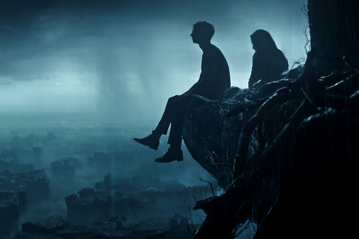 Tom Sturridge as Dream and Kirby Howell-Baptiste as Death sit on the edge of a cliff together looking out into a dark sky in ‘The Sandman’ Season 2.