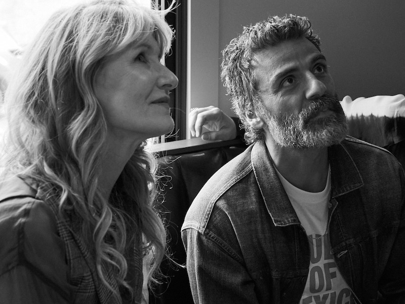 Laura Dern and Oscar Isaac look away from the camera while sitting on a couch.