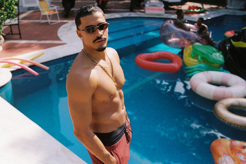 Homem sem camisa posa para foto em frente a uma piscina