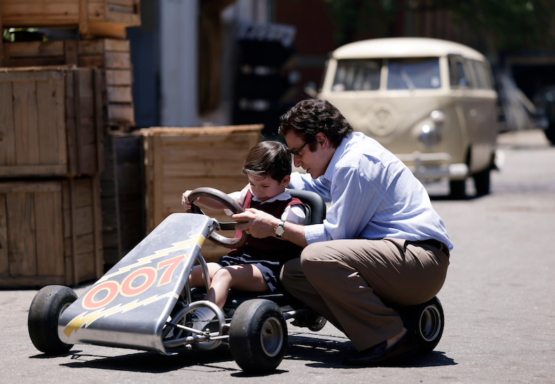 Marco Ricca as Miltão sits with a boy as he drives a toy car in 'Senna'