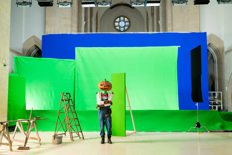 Merv Pumpkinhead (played by Nicholas Anscombe and voiced by Mark Hamill) poses in front of green screens.