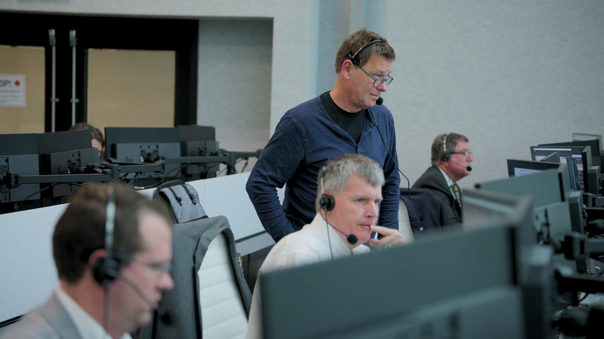 Men wearing headsets stare at computer screens