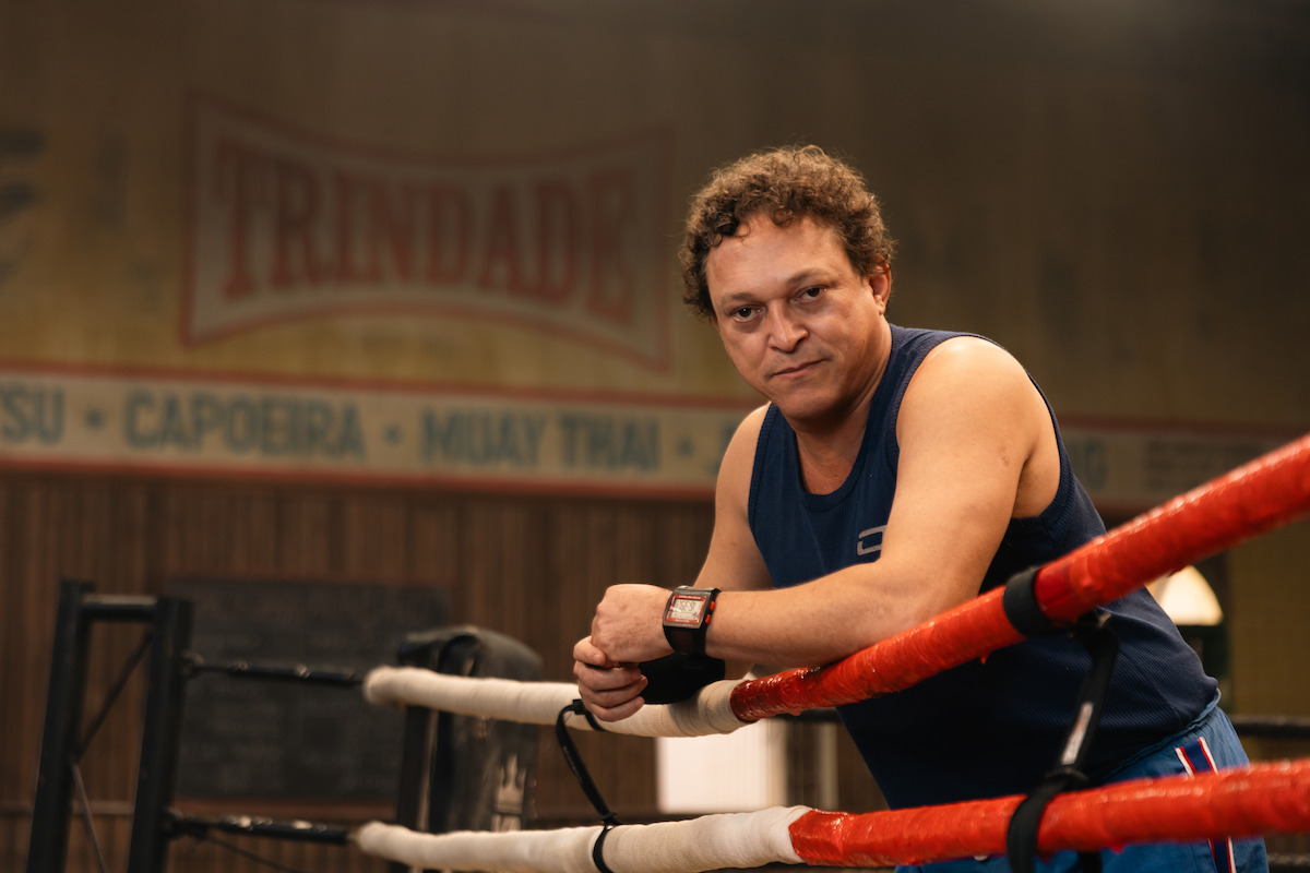 Treinador interpretado por Fábio Lago repousa sobre as cordas de um ringue, em cena da série “Fúria”