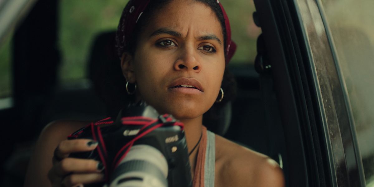 Zazie Beetz as Bo sitting in a car peering out of the window while she holds a large camera in Season 6 of ‘Black Mirror.’