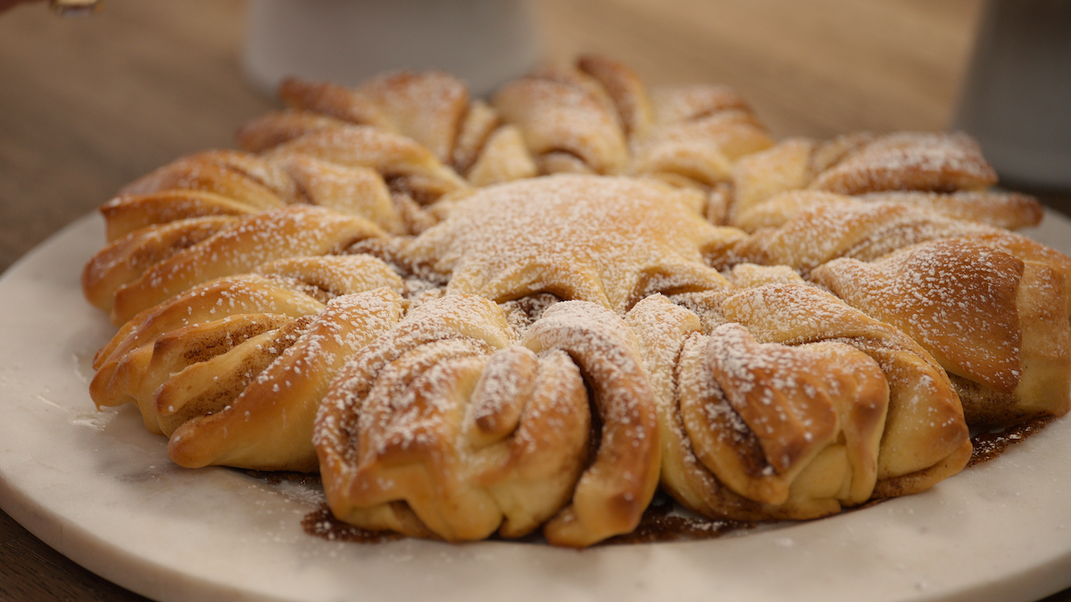 A star-shaped pastry dusted with powdered sugar sits on a round marble platter atop a wooden table, creating a cozy and inviting atmosphere.