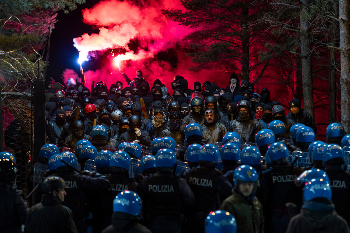 A mass of riot police gathers outside as tear gas plumes can be seen in the background in an image from the series ‘Public Disorder.’