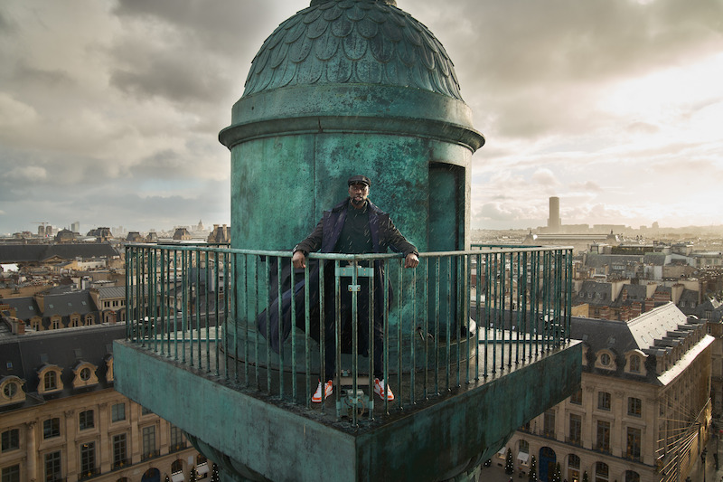 Omar Sy as Assane Diop  stands on the balcony of a high tower in Season 3 of 'Lupin.'