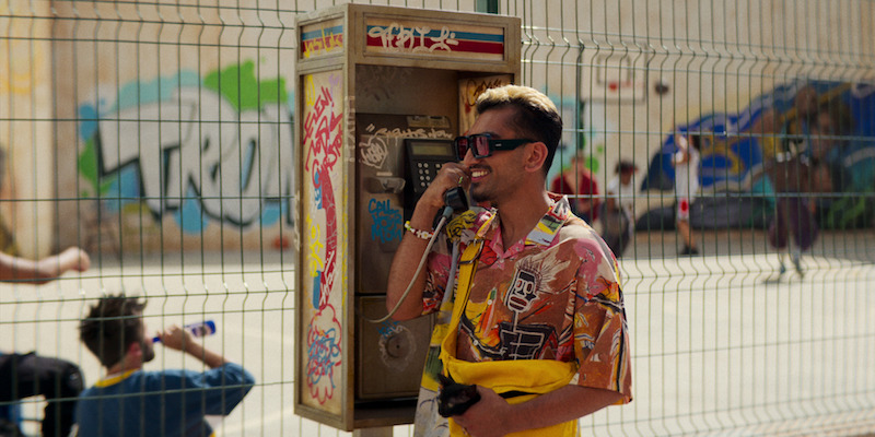 Nabhaan Rizwan as Dionysus smiles talking at a payphone in 'KAOS'