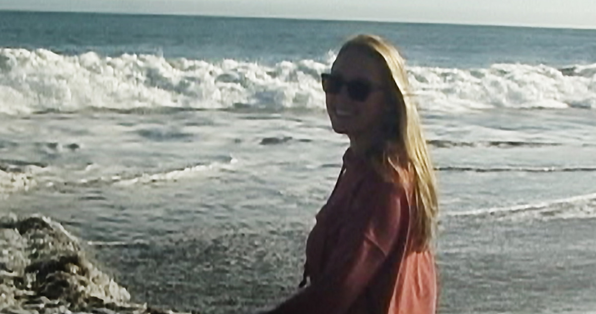 Woman with sunglasses looking at camera with beach in the background.