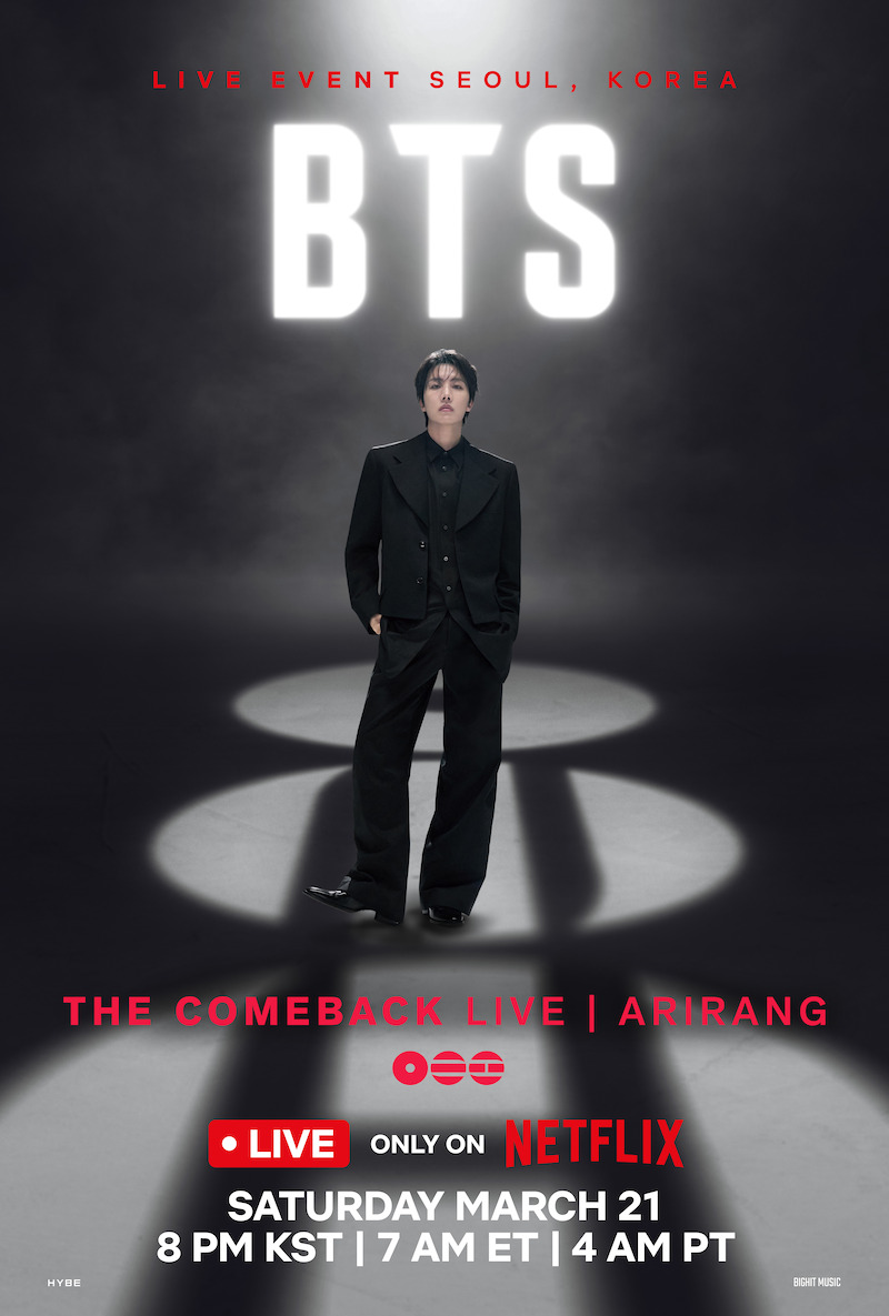 j-hope in a black suit stands under a spotlight with large white "BTS" letters and "Live Event Seoul, Korea" in red above him, all set against a dark background.