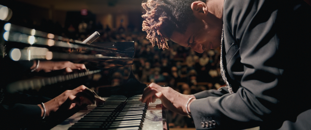 Jon Batiste plays a piano in front of an audience.