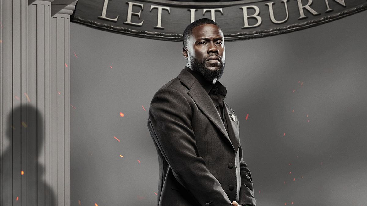 A man in a black suit stands in front of gray columns and a sign reading "LET IT BURN," with embers floating in the air, giving a dramatic and intense atmosphere.