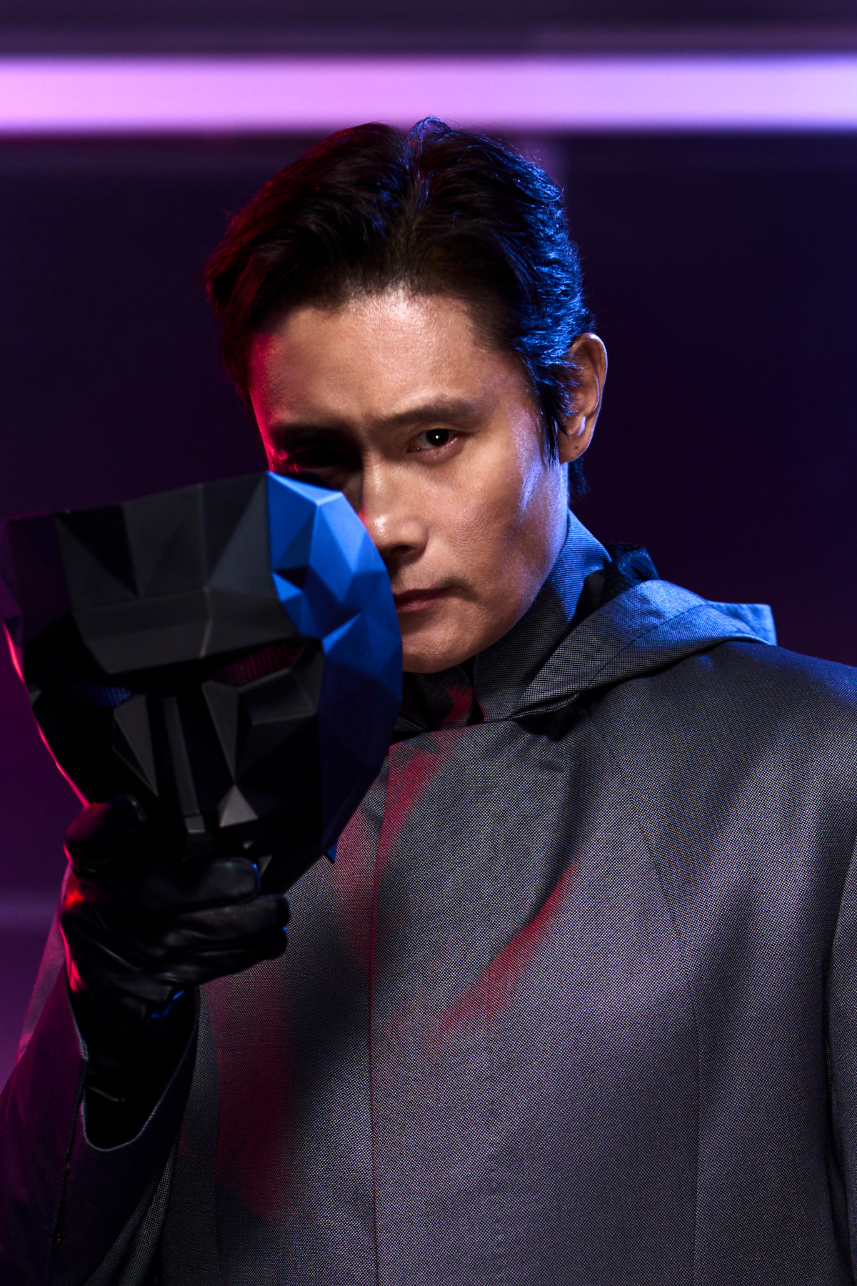 Lee Byung-hun as Front Man in a gray coat and black gloves moves aside a black mask to revel his face in season 2 of ‘Squid Game’