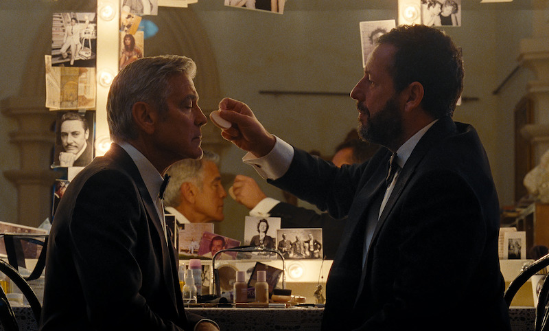 A pulled out shot of Ron Sukenick (Adam Sandler) darkening Jay Kelly's (George Clooney) eyebrows in a dressing room.