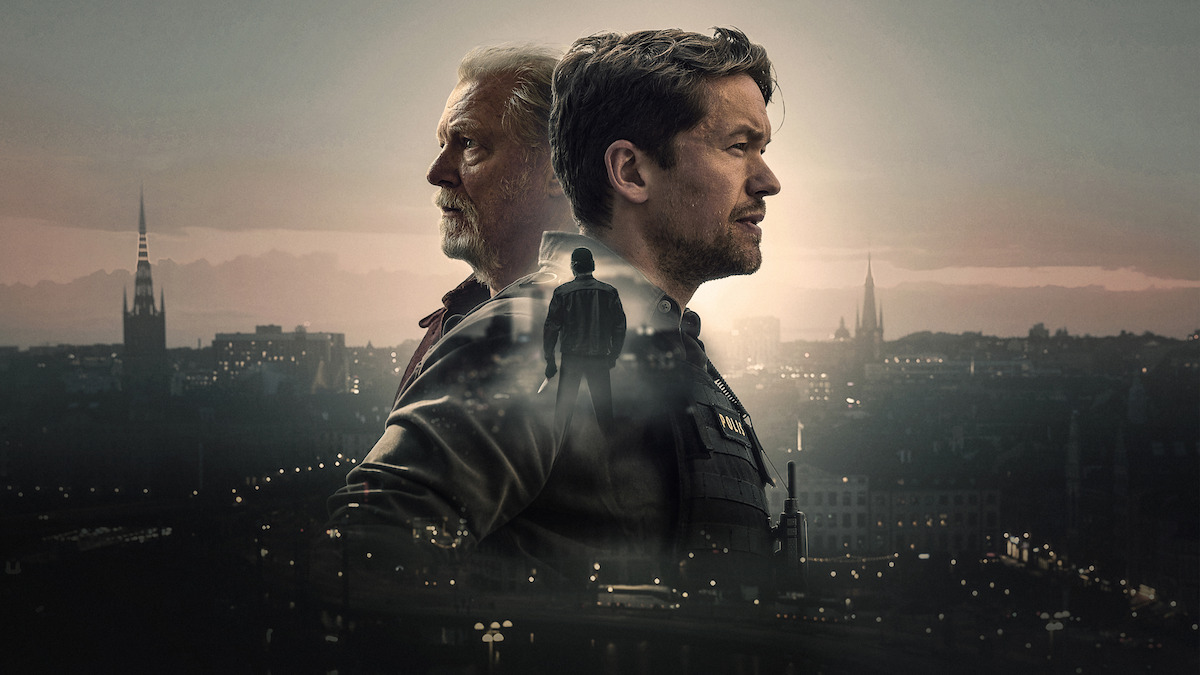 Two men stand back to back against a moody cityscape backdrop at dusk, with a silhouette of a person walking between them, suggesting a dramatic or suspenseful atmosphere in an urban environment.