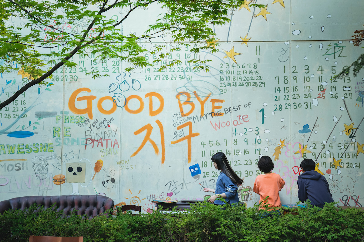 Three children write on a wall filled with graffiti and calendar dates in a still image from the series ‘Goodbye Earth.’