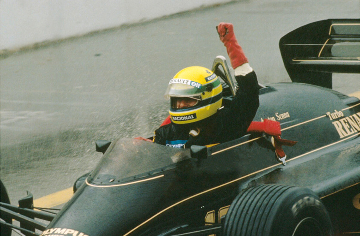 Ayrton Senna wears a yellow helmet and raises his fist out of the cockpit of a shiny forest green car.