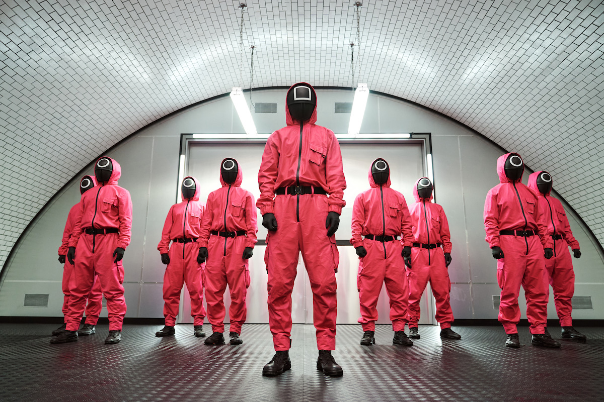 Several masked guards from ‘Squid Game’ standing in front of a metal door