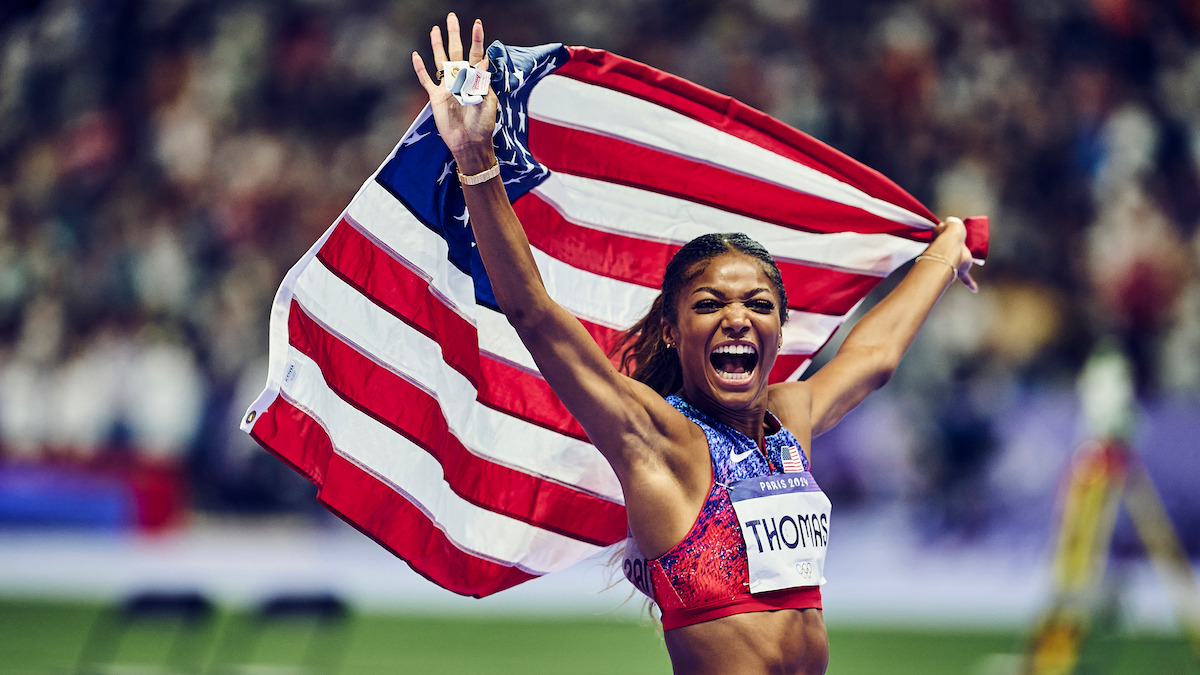 A victorious runner holds the American flag over their head