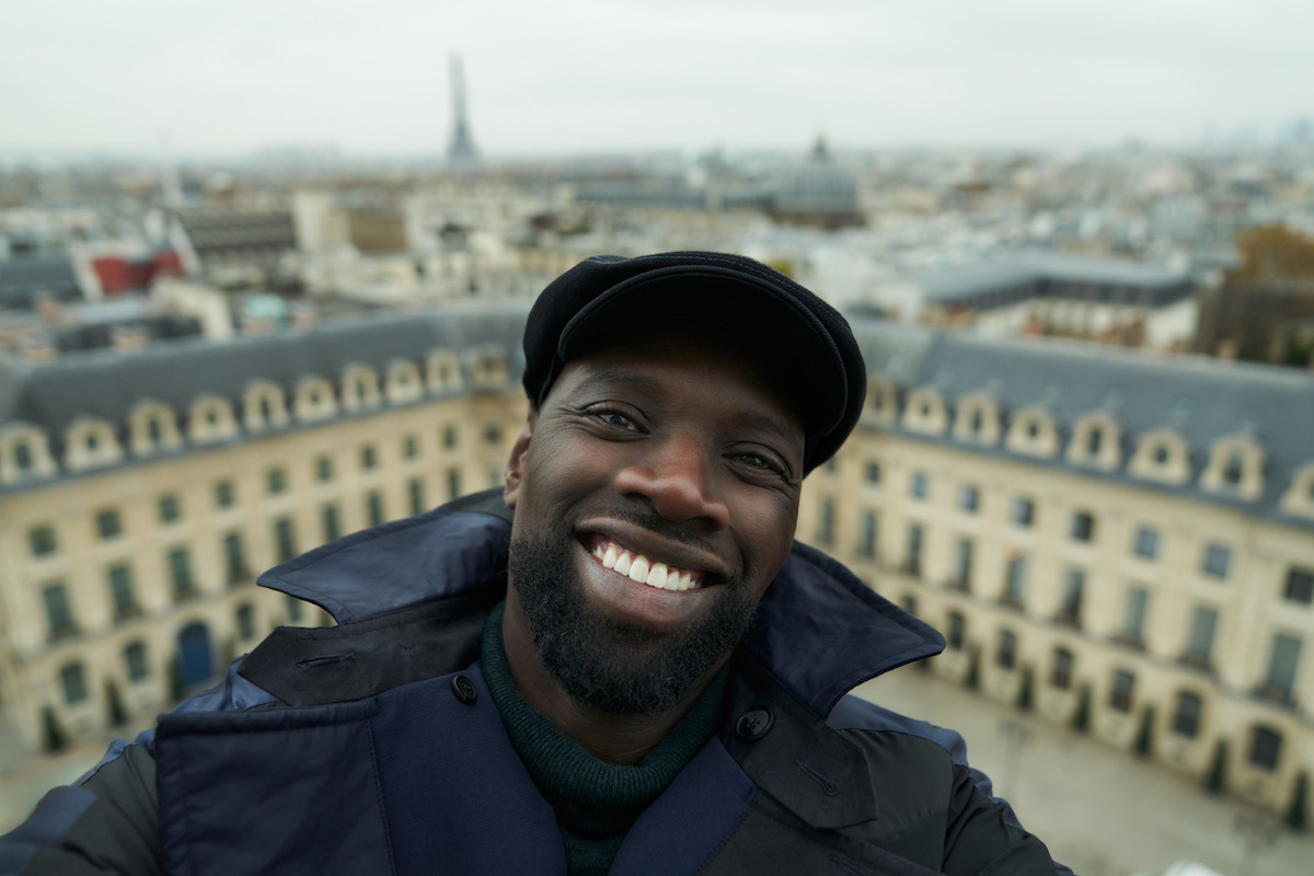 Omar Sy as Assane Diop takes a selfie with the cityscape of Paris in the background in Season 3 of ‘Lupin.’