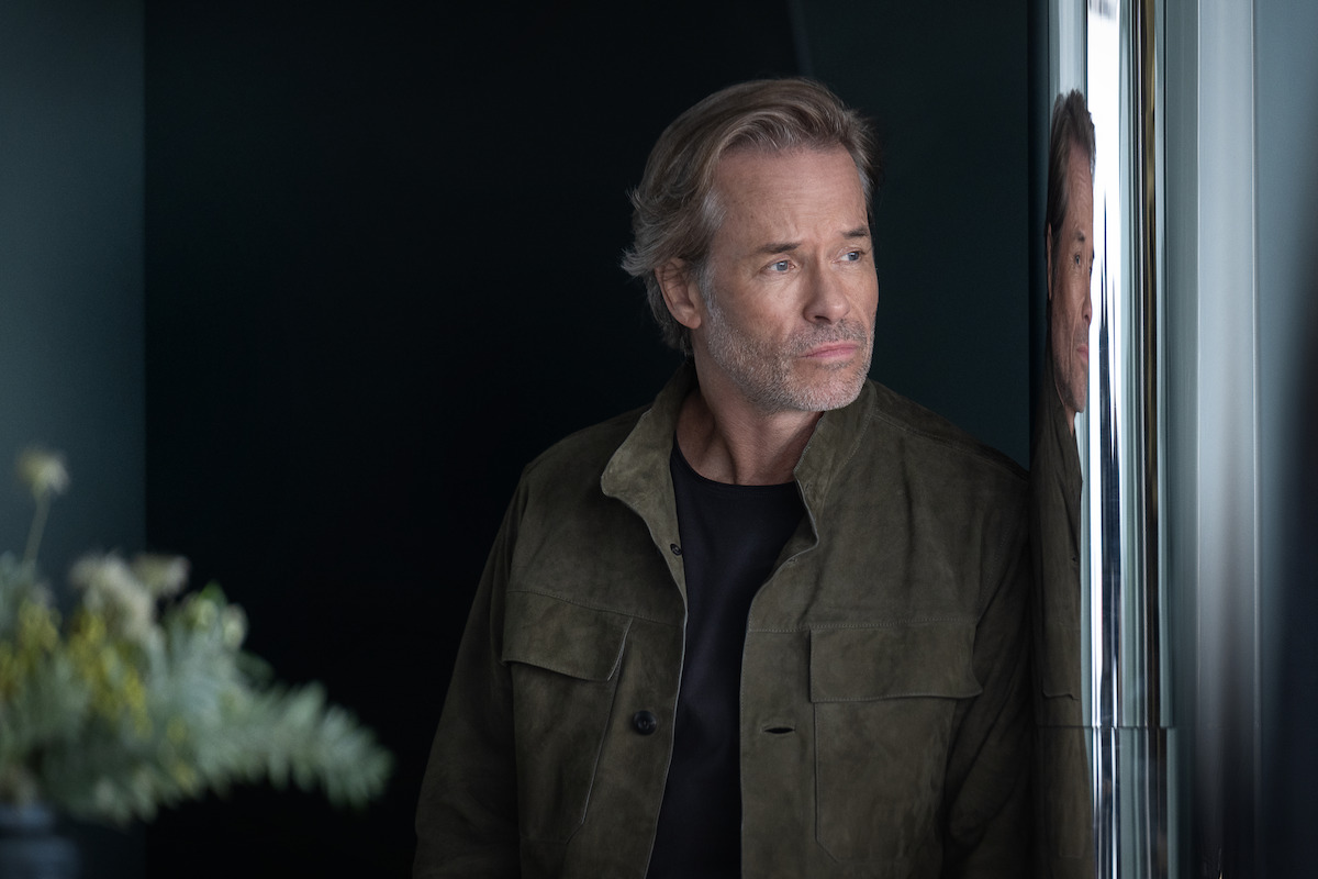 Guy Pearce looks out a window with a concerned expression.