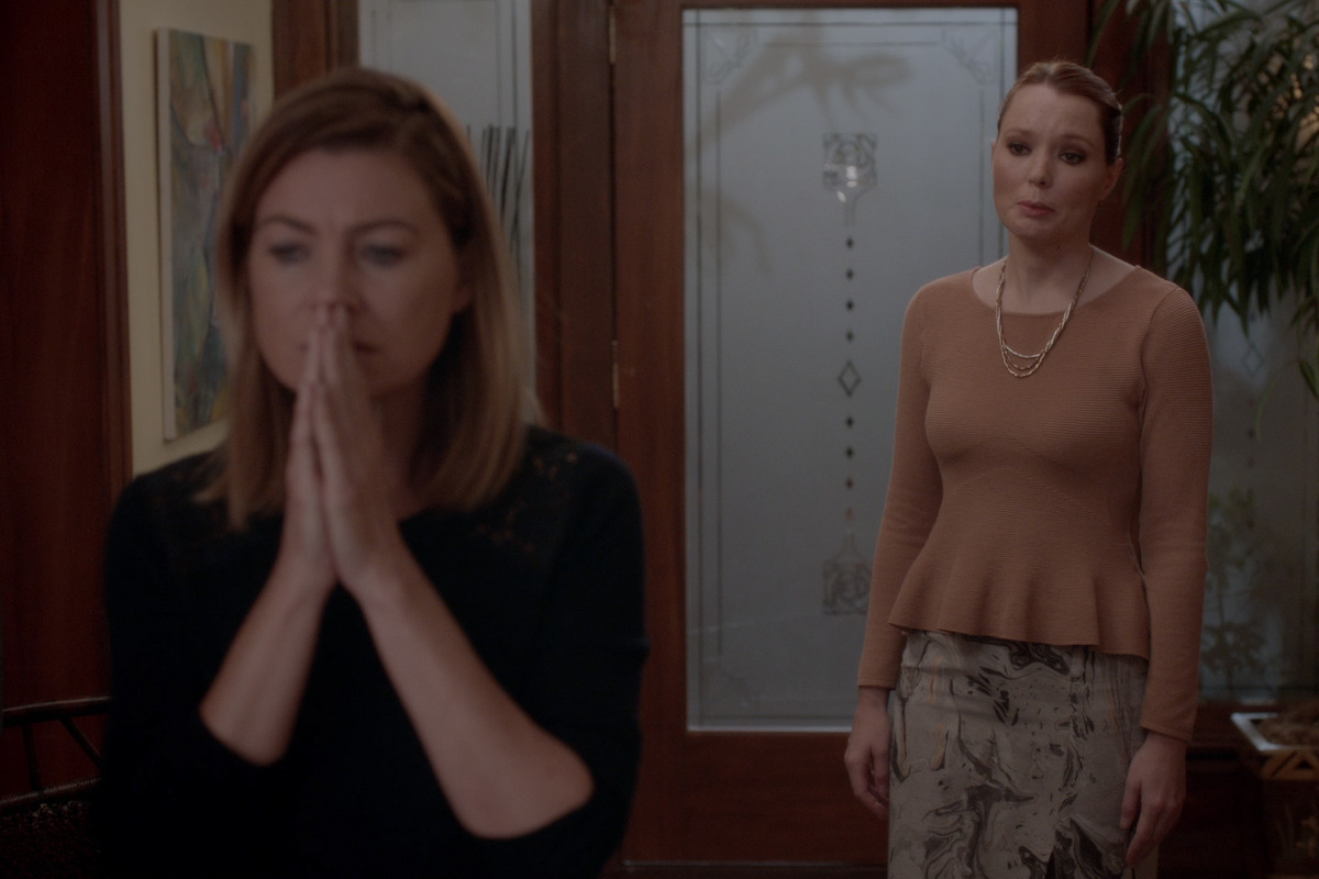 a woman holds her hands in front of her mouth in the foyer of a home while another woman pleads behind her. 