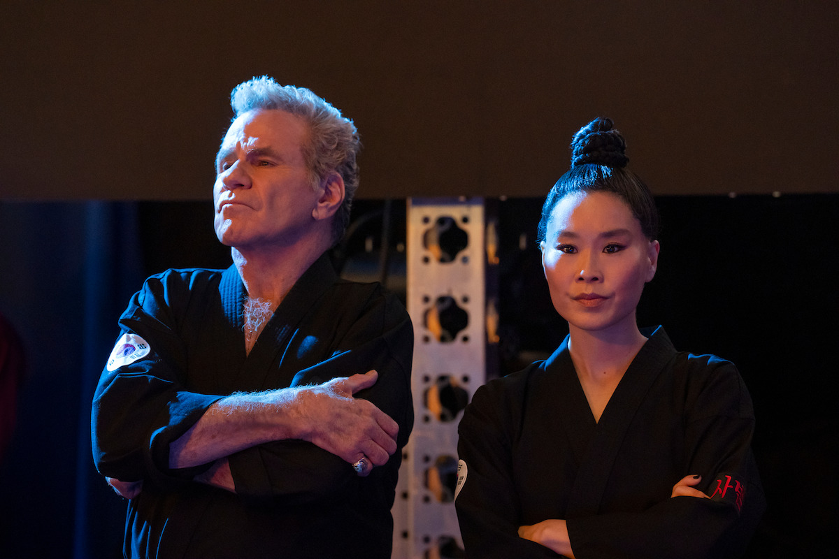 Martin Kove as John Kreese and Alicia Hannah-Kim as Kim Da-Eun fold their arms with disapproving expressions in Season 6 of ‘Cobra Kai’
