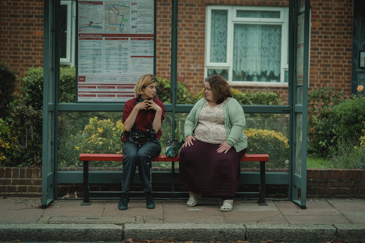 Weronika Tofilska and Jessica Gunning sit on a bus bench.
