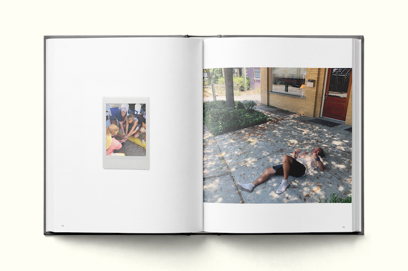 An open photo book showing a small picture of people sitting on the left page, and a large photo of a person lying on a shaded sidewalk outside a brick building on the right page.