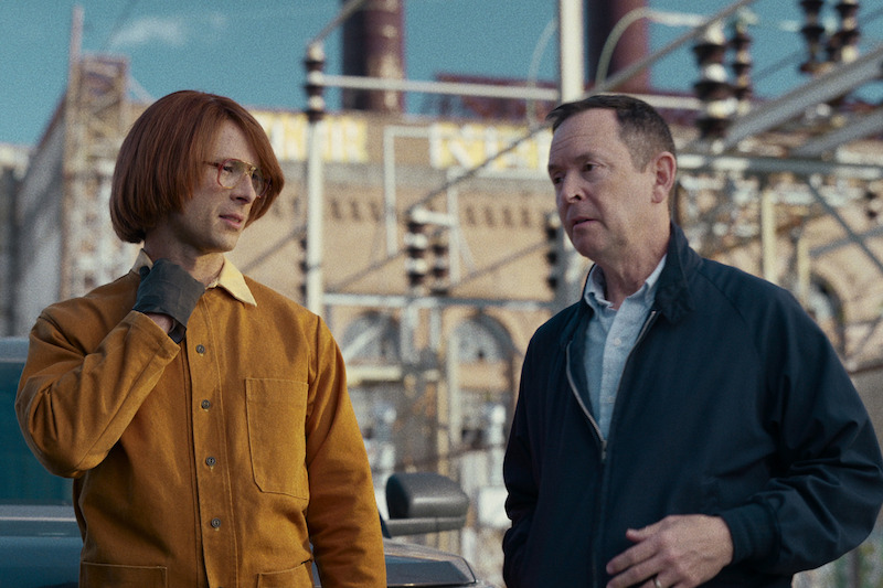 Gary Johnson (Glen Powell) undercover with a client. Johnson wears a Carhart jacket and orange wig. His client wears a dark jacket and looks nervous.
