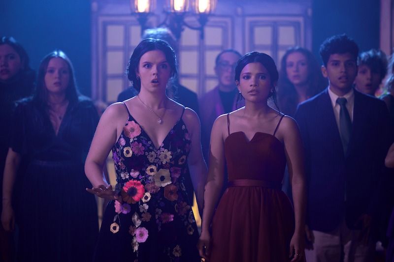 Ellie O’Brien as Grace and Nikki Rodriguez as Jackie wearing dresses in a crowd in 'My Life with the Walter Boys' Season 2