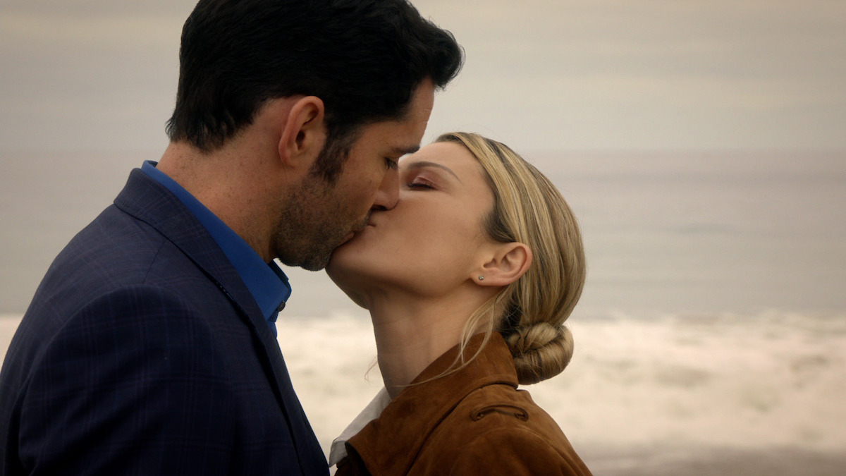 A man and a woman kiss on a beach, with ocean waves and a cloudy sky in the background, creating a romantic and intimate moment.
