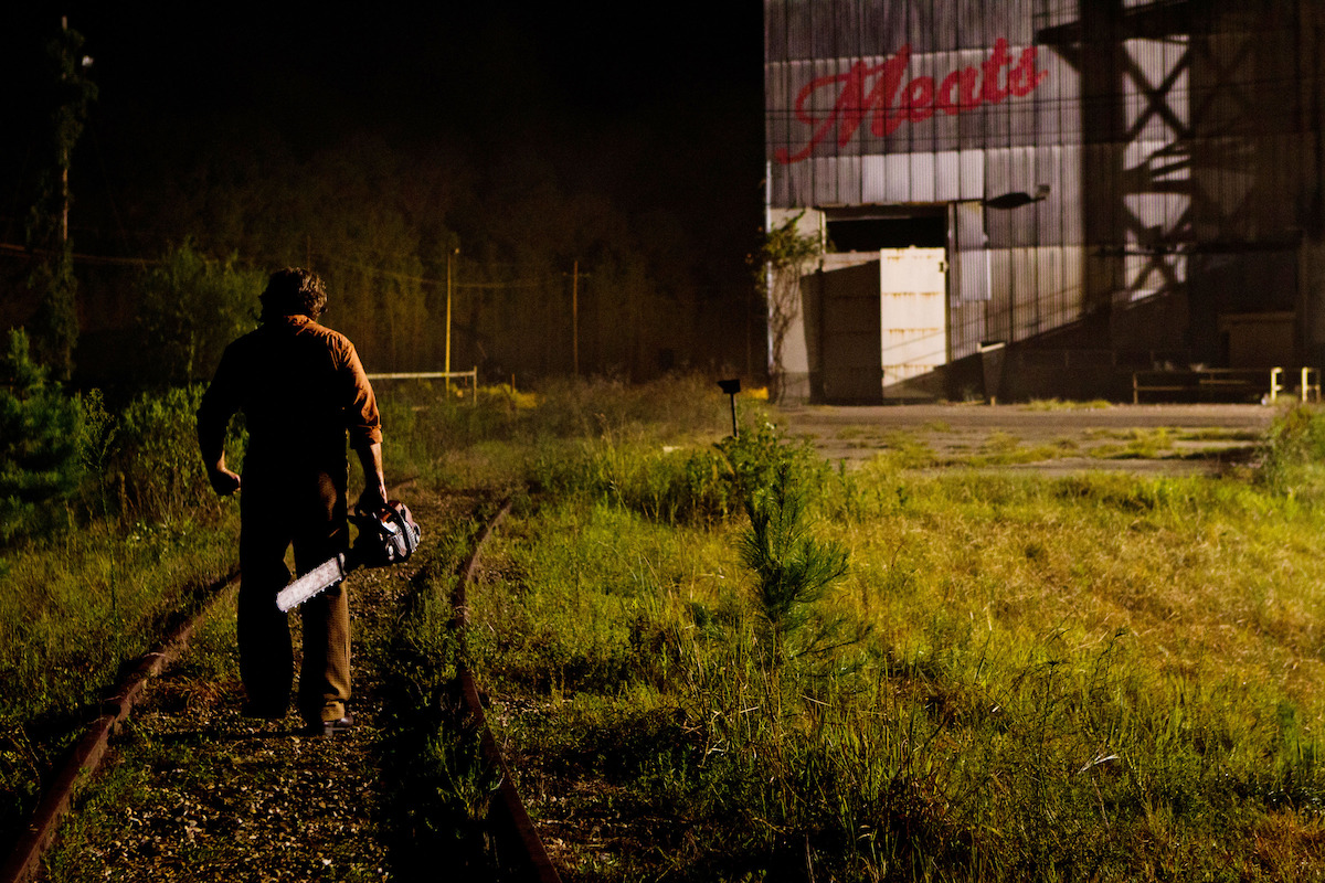 Leatherface headed toward a barn with a chainsaw