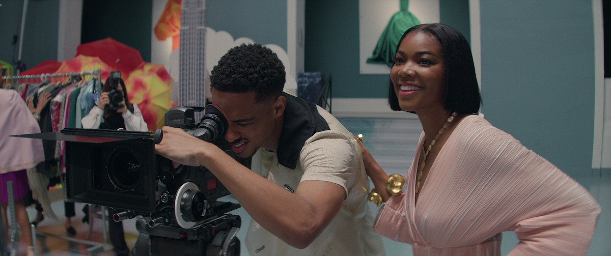 Gabrielle Union wears a pink pleated dress standing next to Keith Powers as he films in a still from ‘The Perfect Find.’