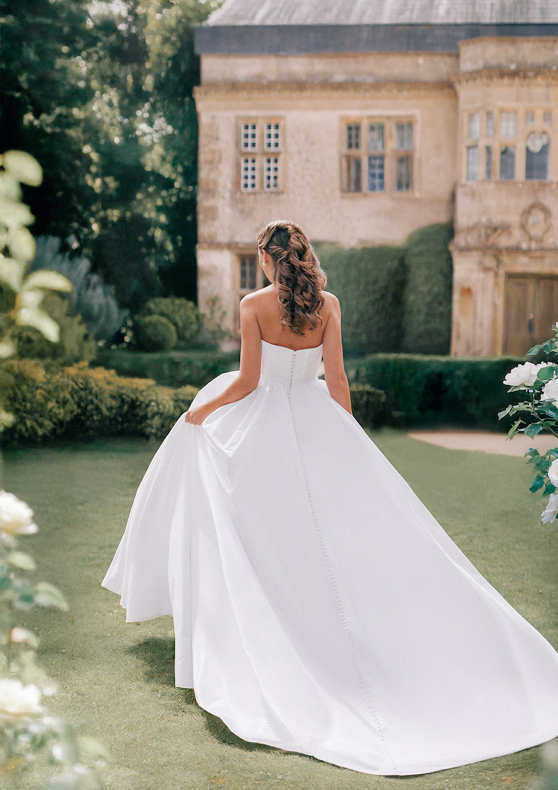 Woman in bridal dresses poses and looks off into the distance.