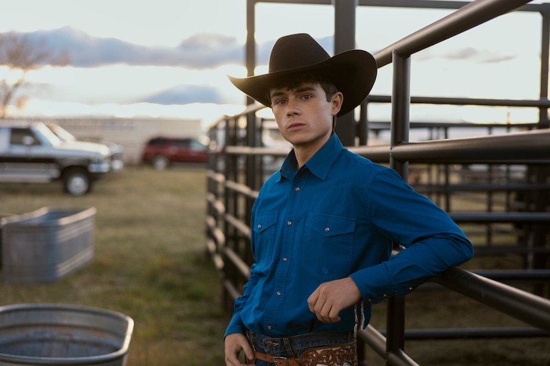 Gentry as Alex wearing a cowboy hat and blue shirt at a ranch in 'My Life with the Walter Boys' Season 2