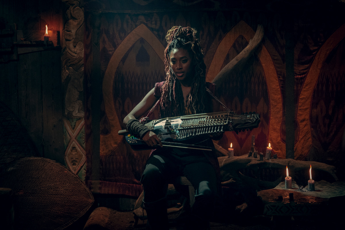 Éile (Sophia Brown) holding an instrument.