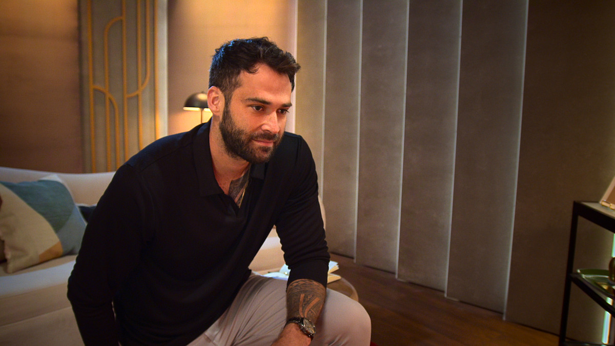 Alex Henderson sitting on couch in modern living room with warm lighting, neutral colors, and decorative elements in the background.