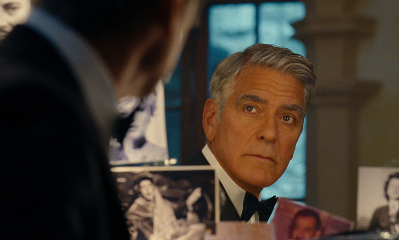 Jay Kelly (George Clooney) stares into a mirror in a dressing room, analyzing not only his appearance but having a moment of calm introspection before an event honoring his career in film.