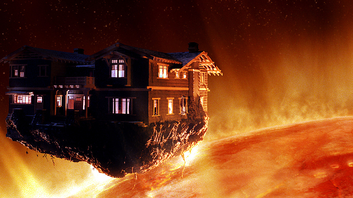 A house perched on a rocky ledge floats dangerously close above the surface of a fiery sun in space, with bright orange flames and intense heat surrounding the scene.