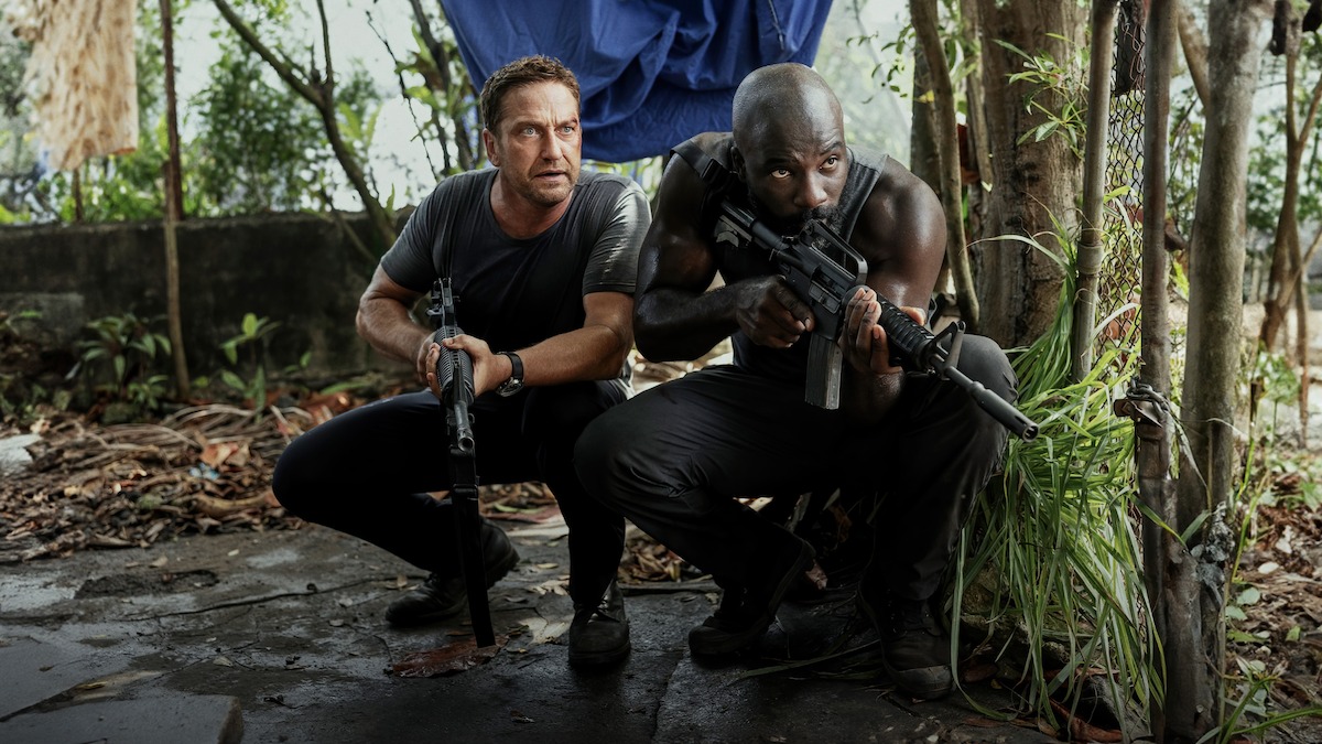 Gerard Butler and Mike Colter crouch down while holding guns in a still image from ‘Plane.’