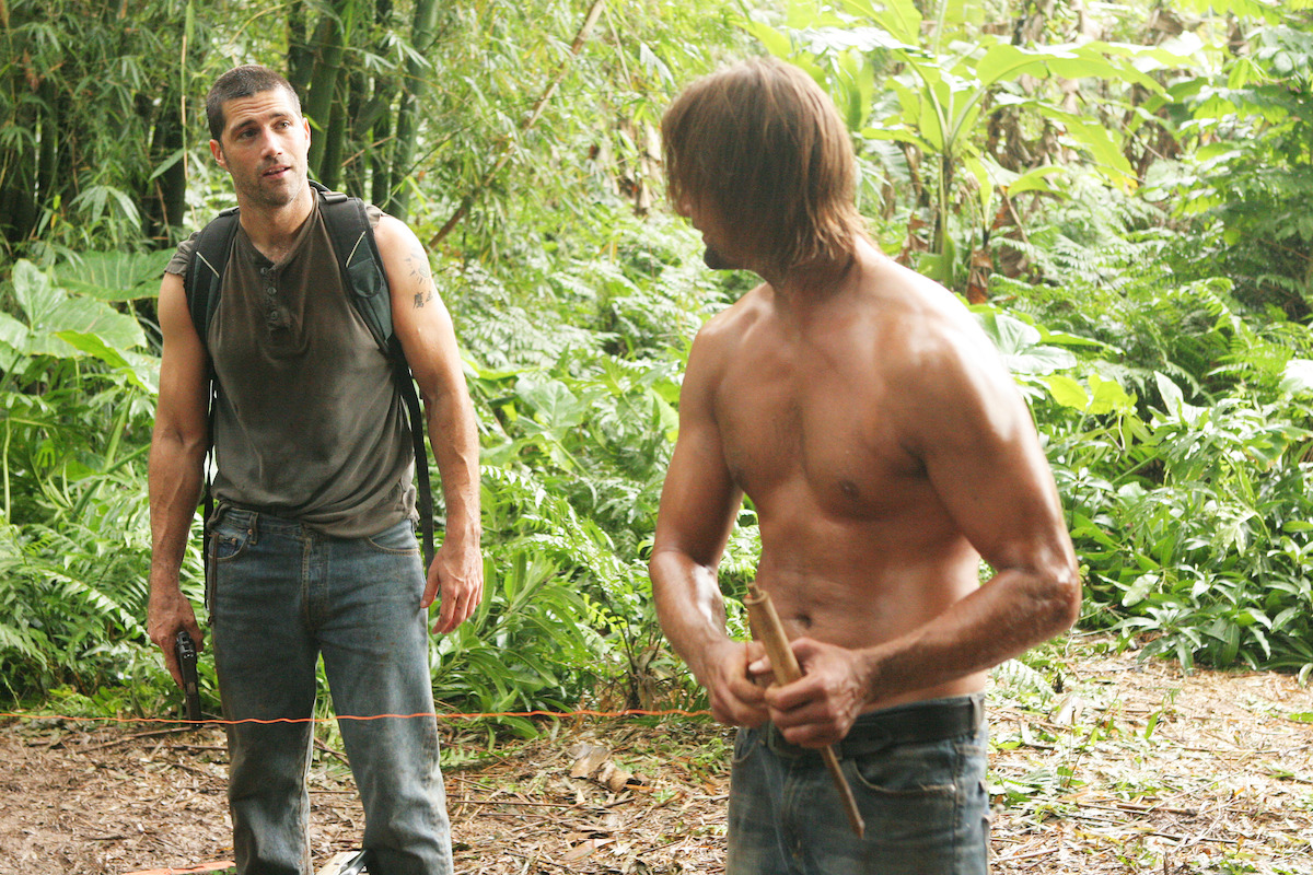 Matthew Fox looking at a shirtless Josh Holloway who is working on a tripwire in the jungle.