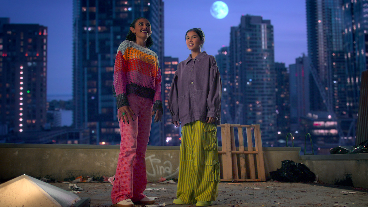 Aaliyah Cinello as Madison and Kaileen Angelic Chang as Carmie stand on a rooftop with the moon glowing behind them in Season 1 of ‘I Woke Up a Vampire.’