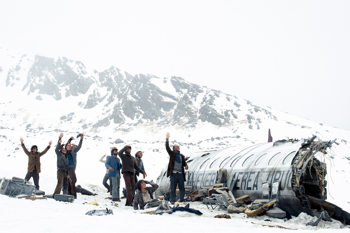 Several people standing in the snow next to an airplane crash