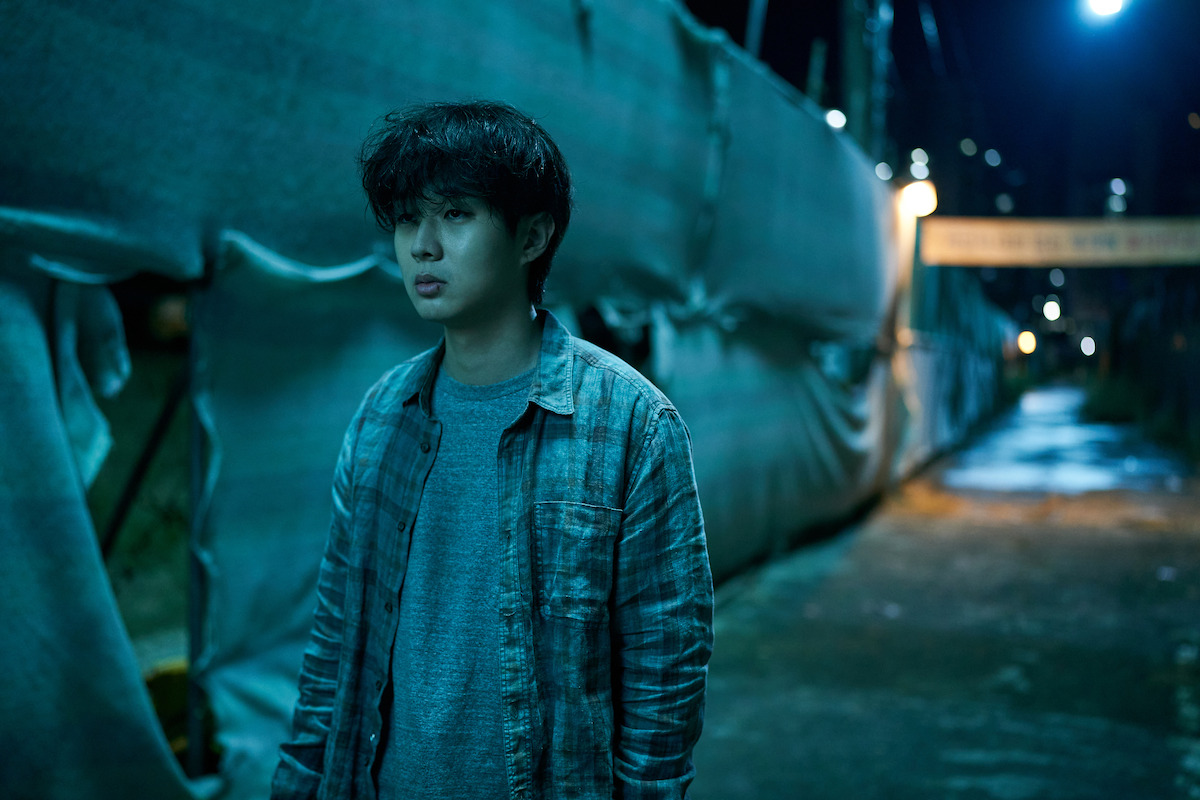 Choi Woo-shik as Lee Tang stands on a street at night in a still image from the series ‘A Killer Paradox’