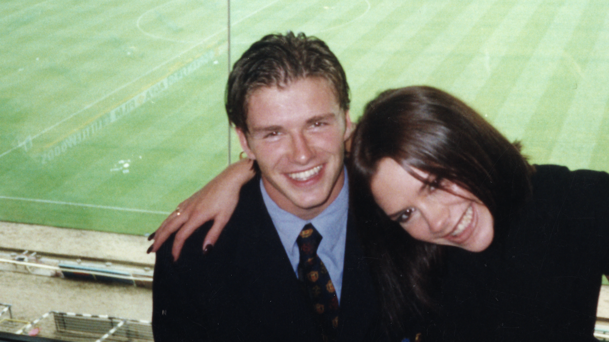 Victoria Beckham with her arm around David in the stands of a football stadium. 