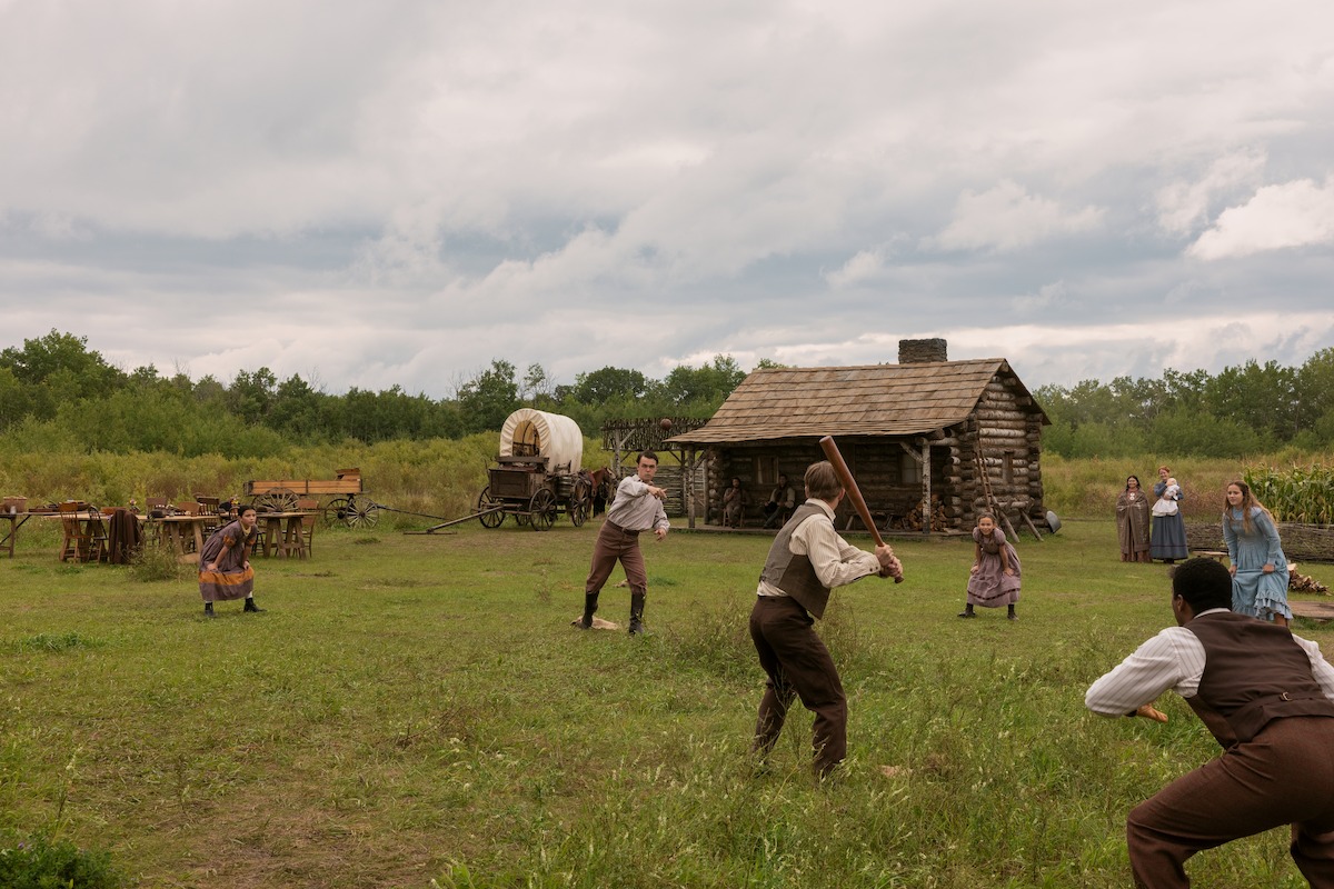 A group of people play baseball in front of a cabin.