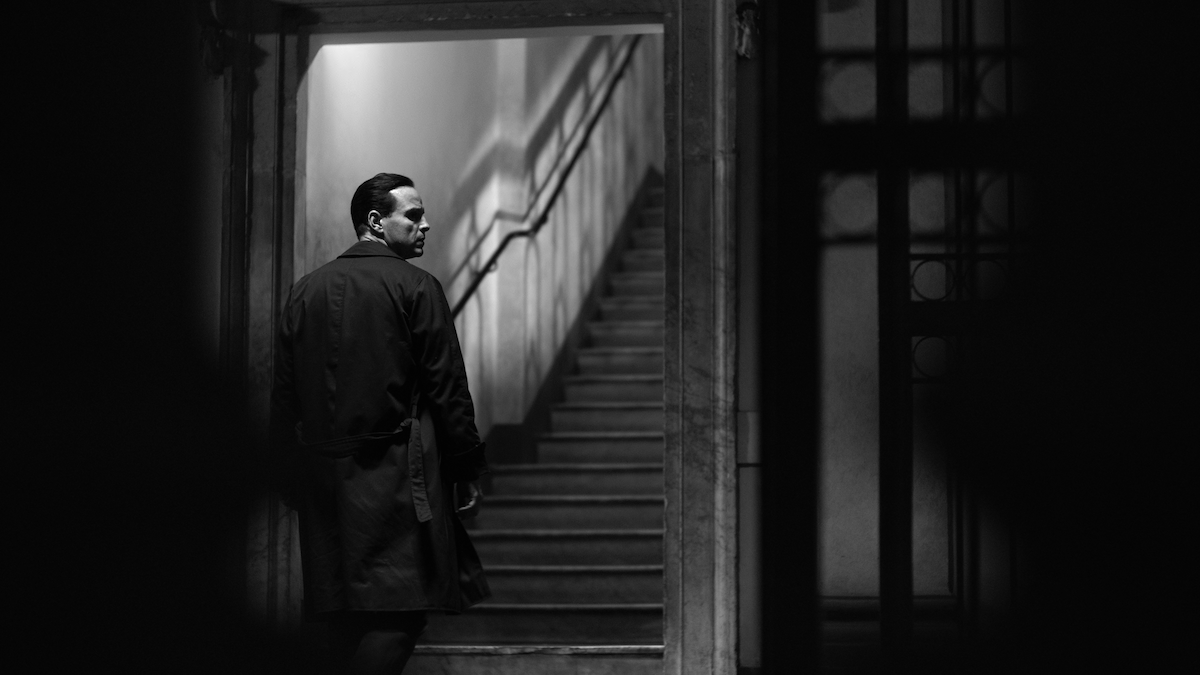 Black-and-white photo of Andrew Scott as Tom Ripley looking over his shoulder before walking up a flight of stairs in ‘Ripley’